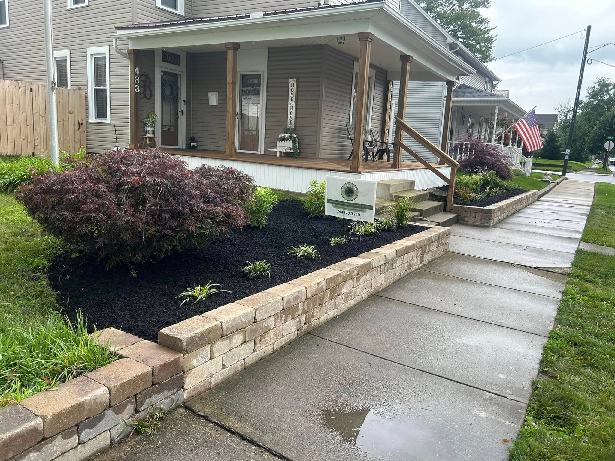 Front yard landscaping with shrubs, flowers, and a concrete walkway by a residential home.
