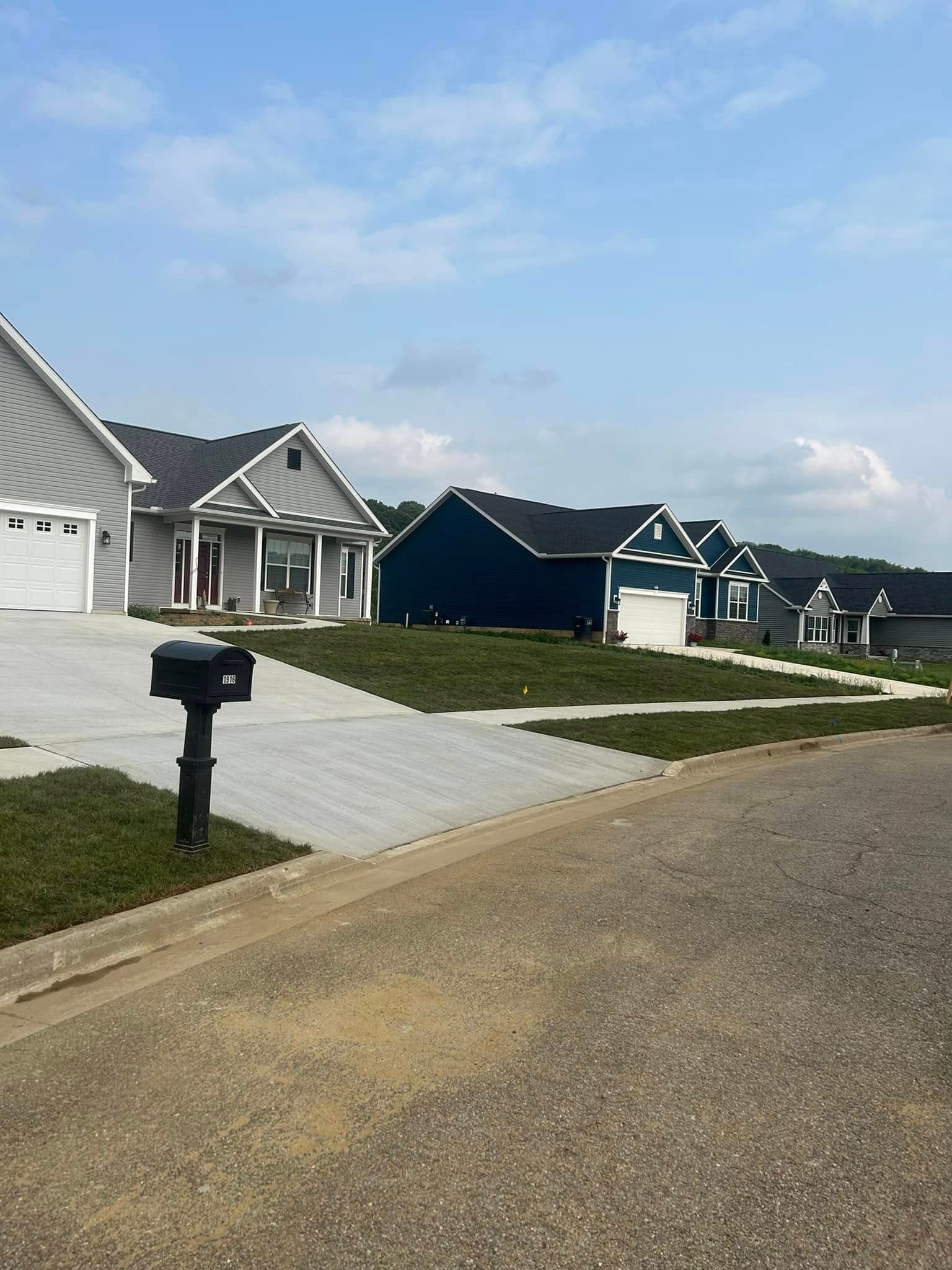 New residential neighborhood with modern homes and a clear blue sky. Paved driveway and mailbox visible.