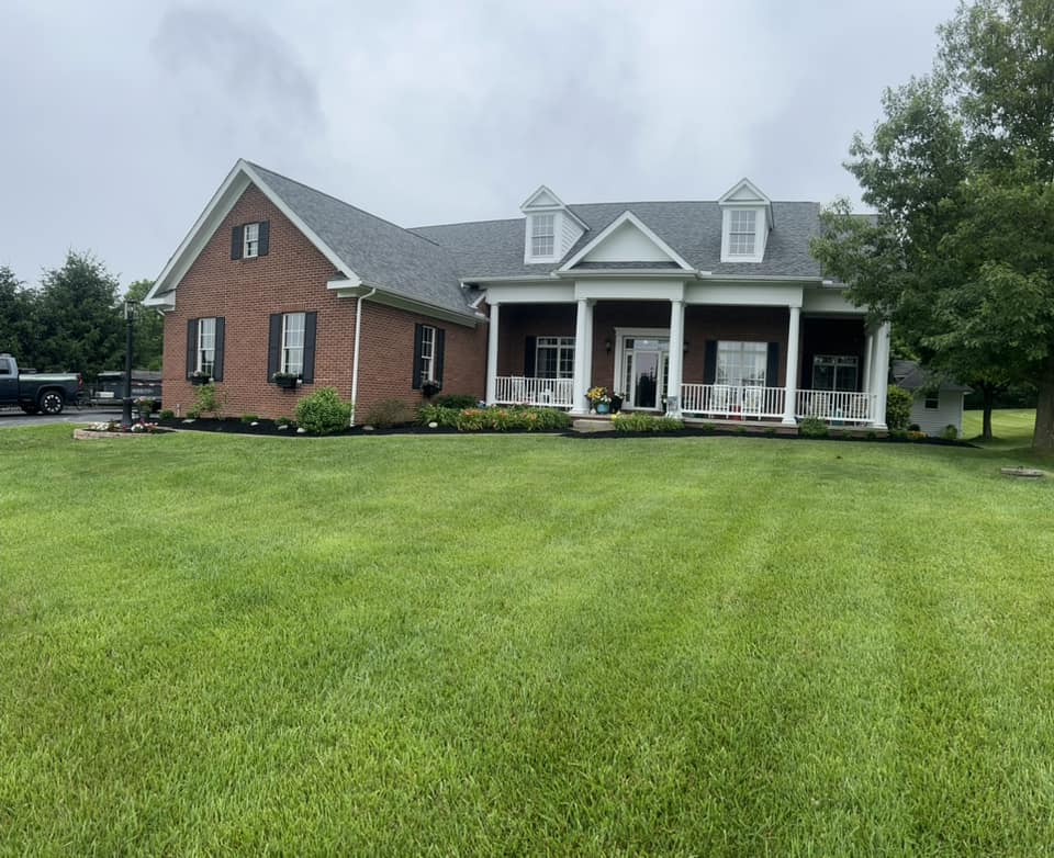 Elegant brick house with a porch, surrounded by lush green lawn and landscaping.