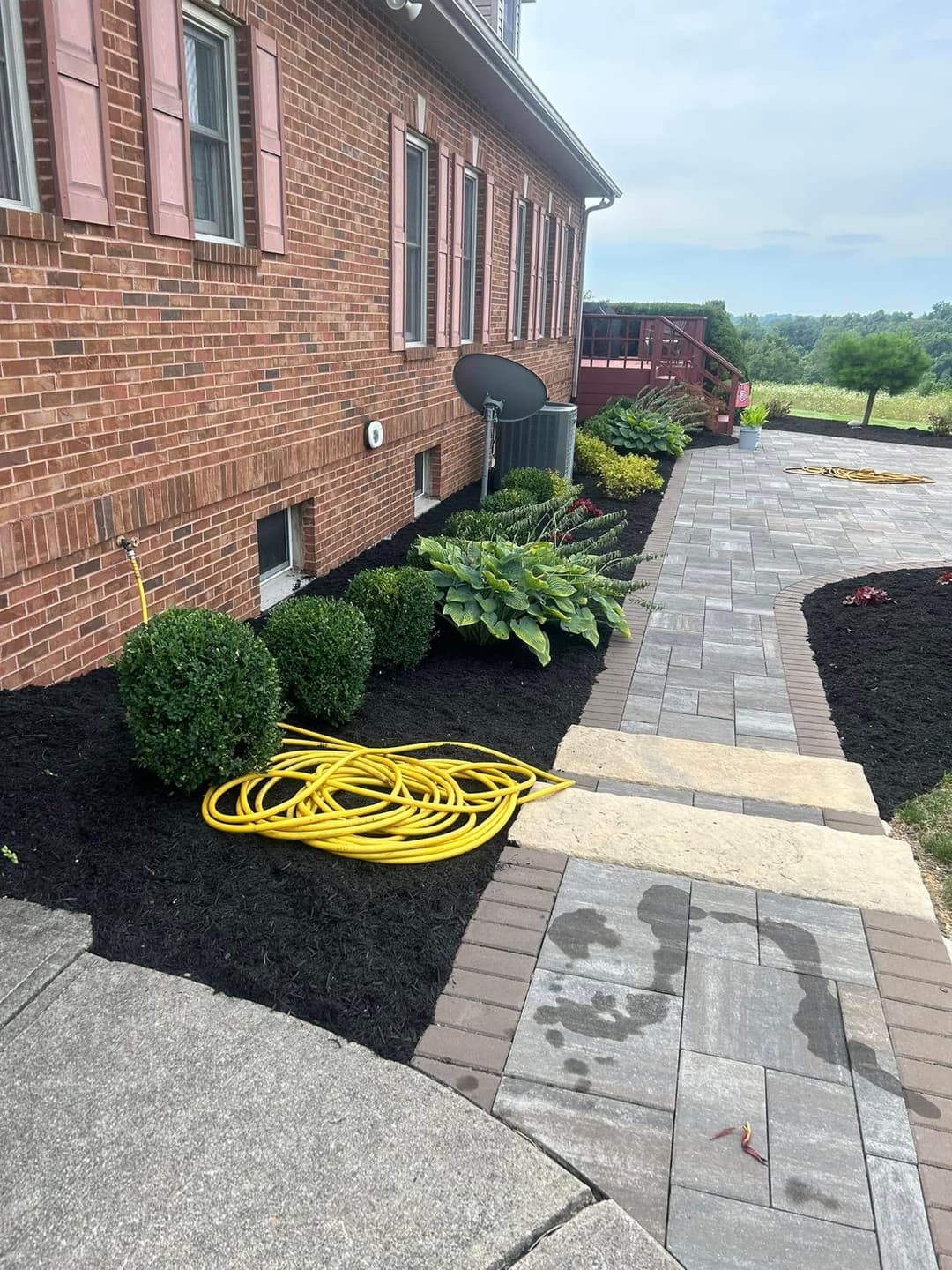 Well-maintained garden pathway with brick pavers and lush greenery beside a brick house.