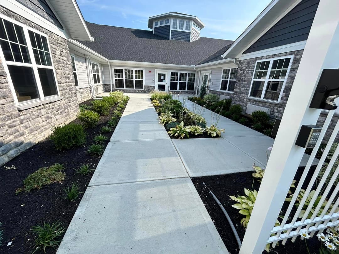 Modern building entrance with landscaped garden paths and greenery, sunny day.
