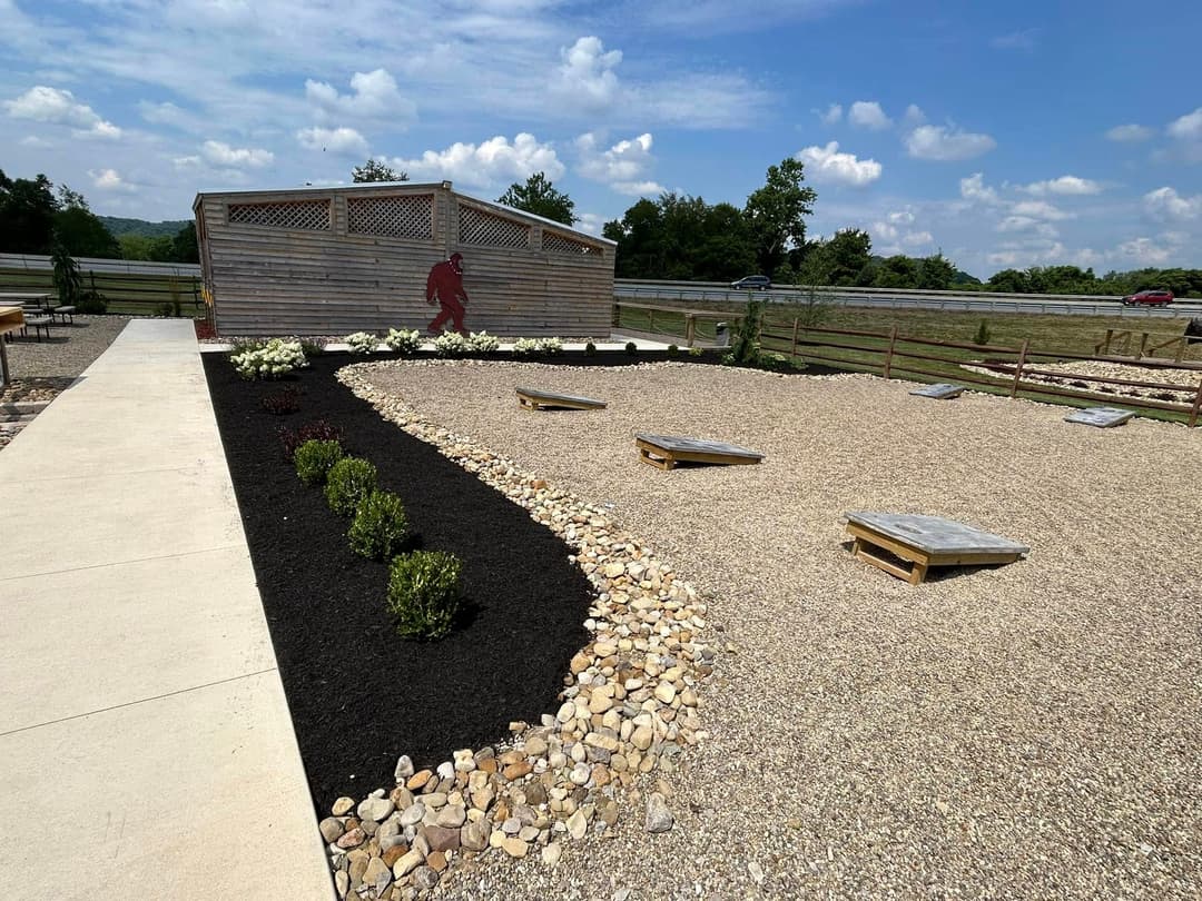 Outdoor recreational area with cornhole boards, gravel landscaping, and a wooden shelter.