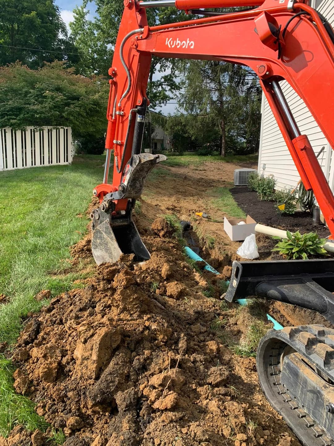 Kubota excavator digging trench in residential yard for landscaping or utility installation.
