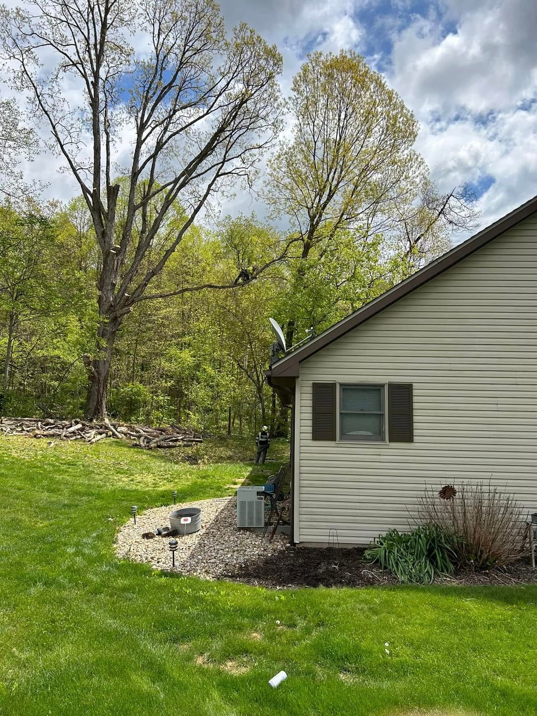 House exterior with landscaping, large tree, and equipment near a lush green yard.