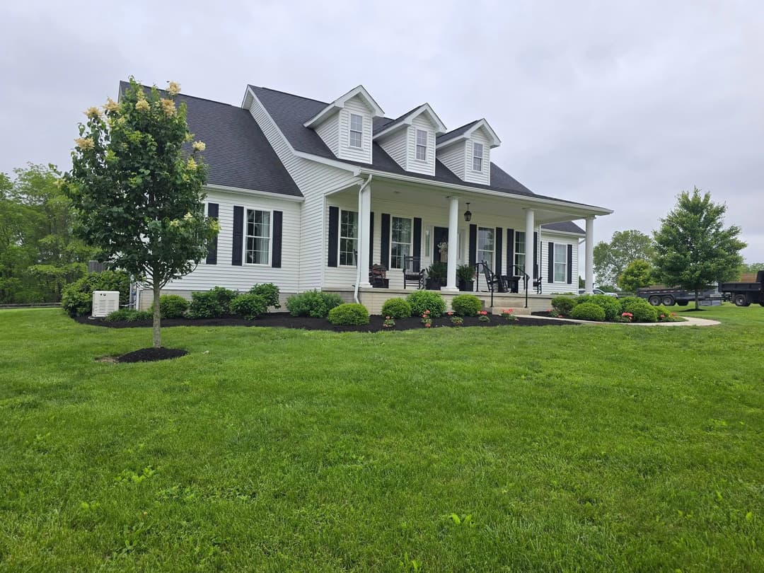 Charming white house with a porch, landscaped yard, and lush green grass on a cloudy day.