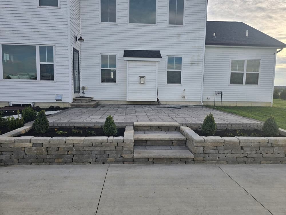 Modern home exterior with stone patio, landscaped garden, and concrete driveway.