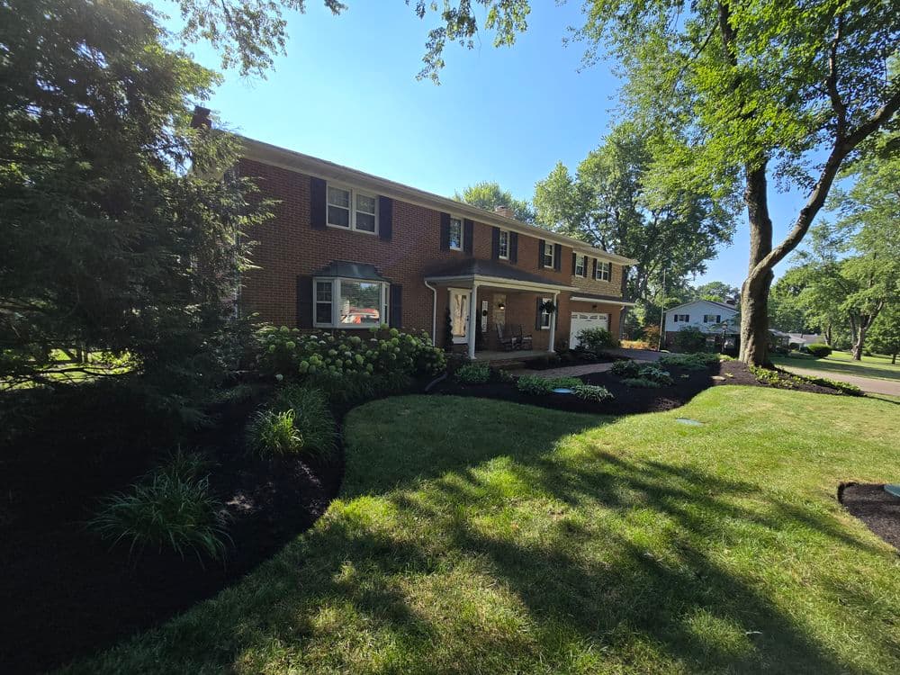 Charming brick home surrounded by lush greenery and landscaped yard on a sunny day.