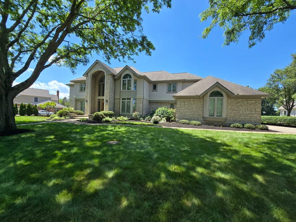 Modern luxury home with stone exterior, large windows, and lush green landscaping.