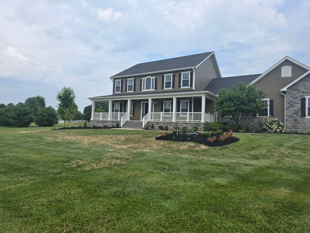 Two-story suburban home with a porch, landscaped yard, and cloudy sky background.