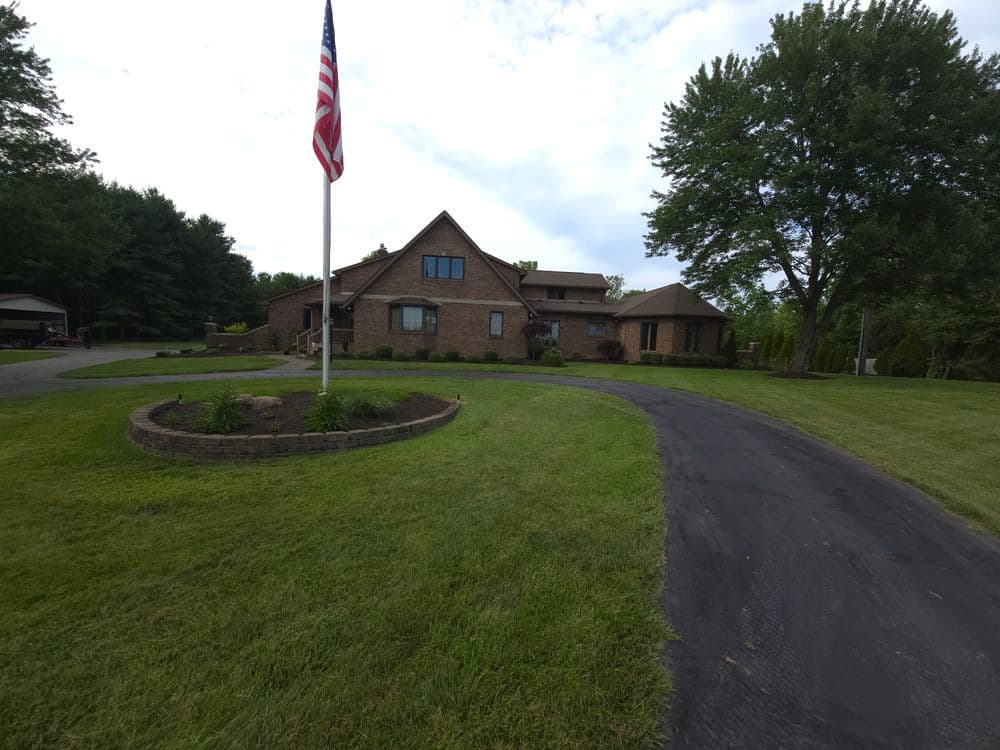Spacious brick house with American flag and landscaped yard on a sunny day.