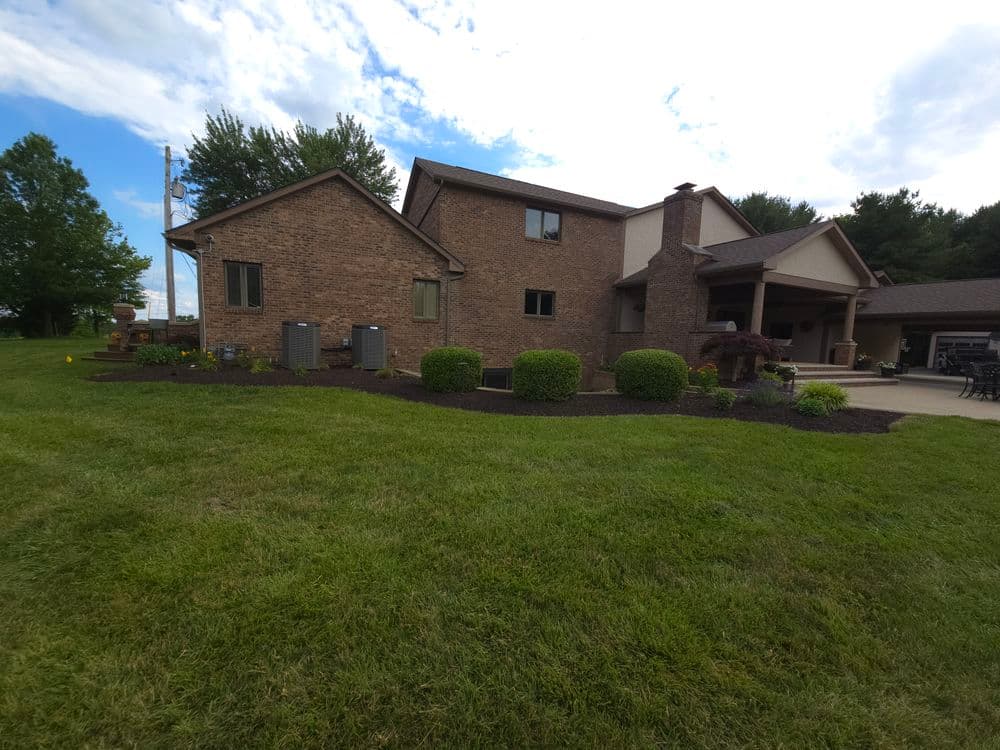 Modern brick house with landscaped yard, green grass, and blue sky in the background.