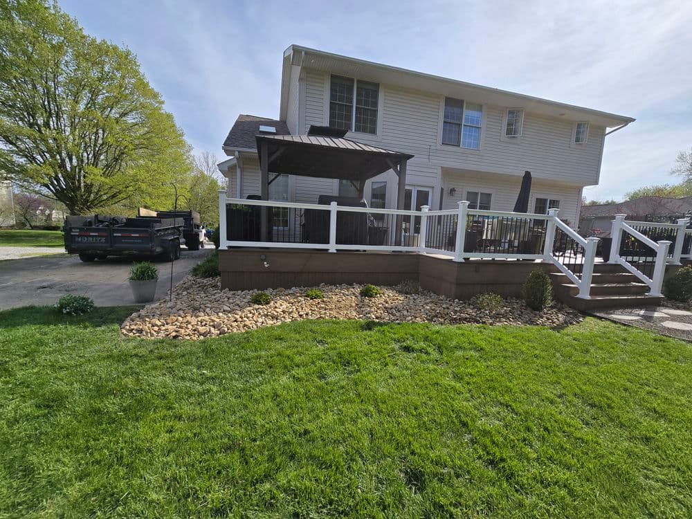 Backyard view of a house with a deck, gazebo, green lawn, and stone landscaping.
