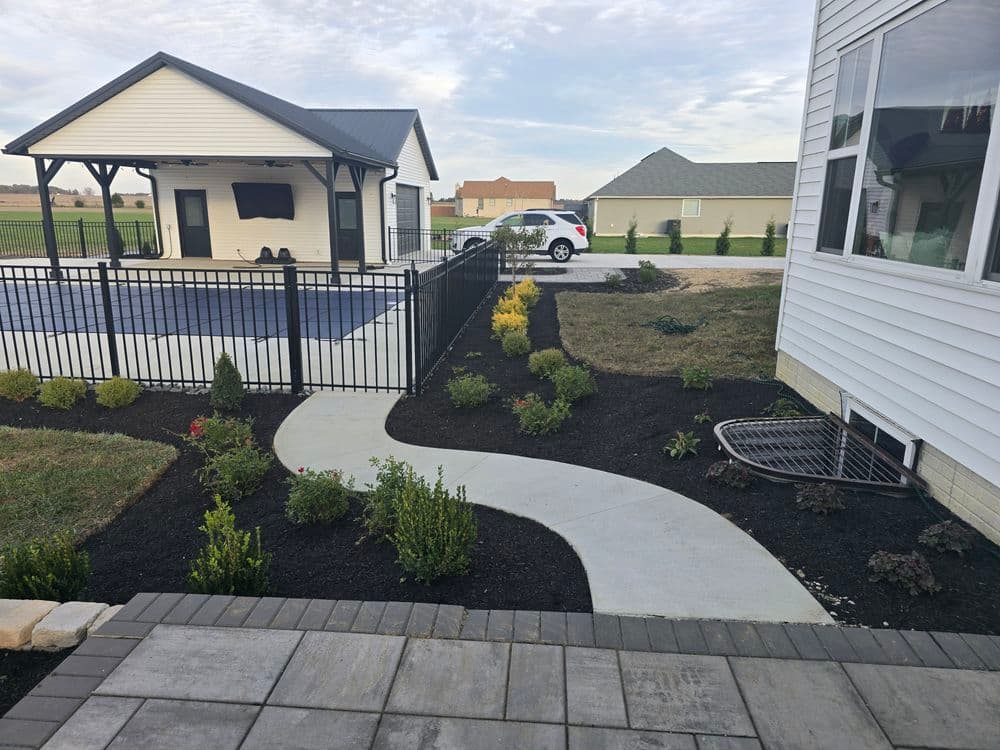 landscaped pathway leading to a modern home and outdoor sports area with fence and greenery.