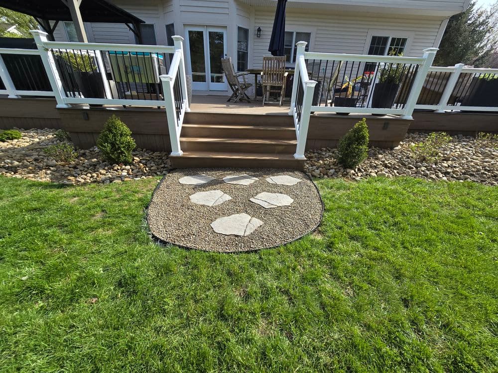 Stone pathway leading to a cozy deck with seating, surrounded by greenery and landscaping.