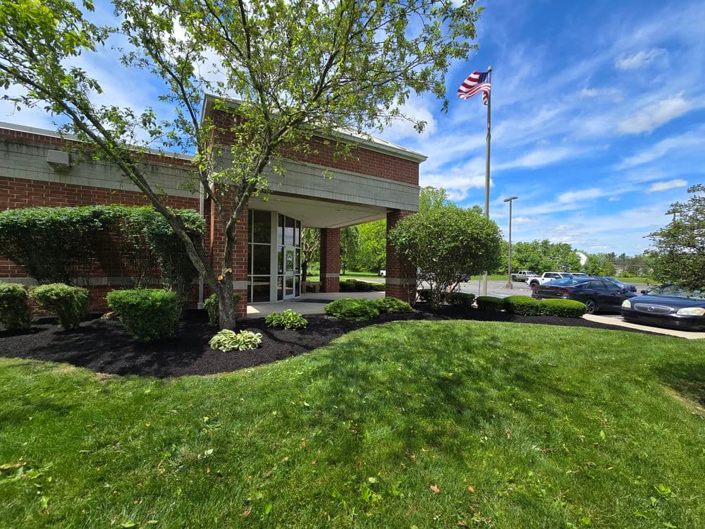Front entrance of a brick building with landscaped greenery and an American flag.