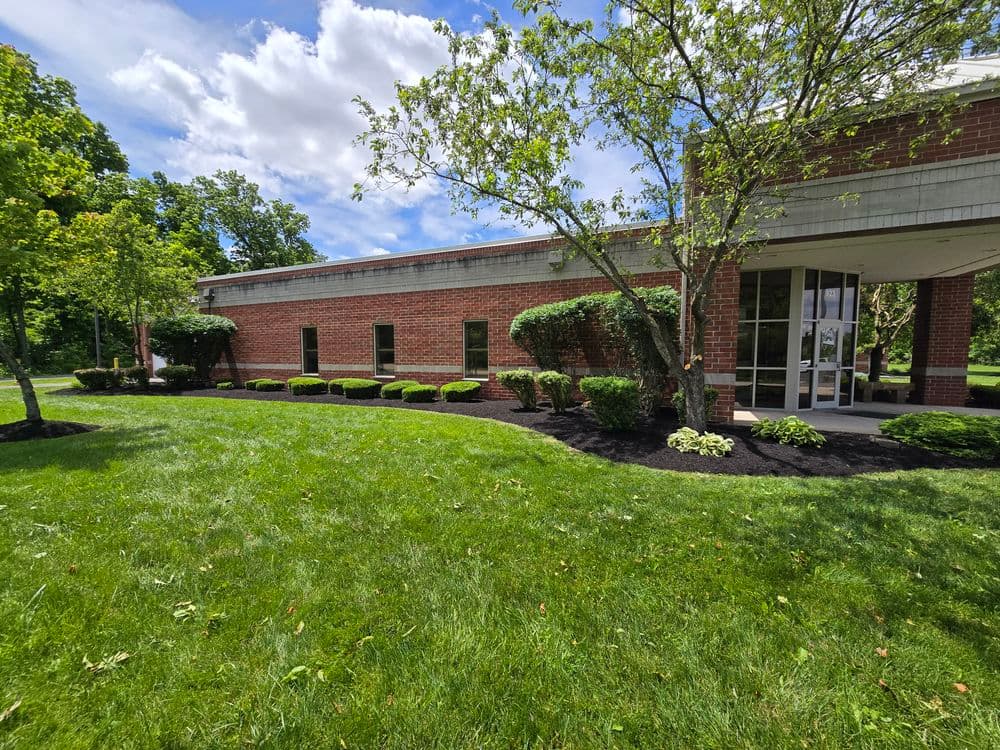 Brick building surrounded by lush green grass and trees on a sunny day.
