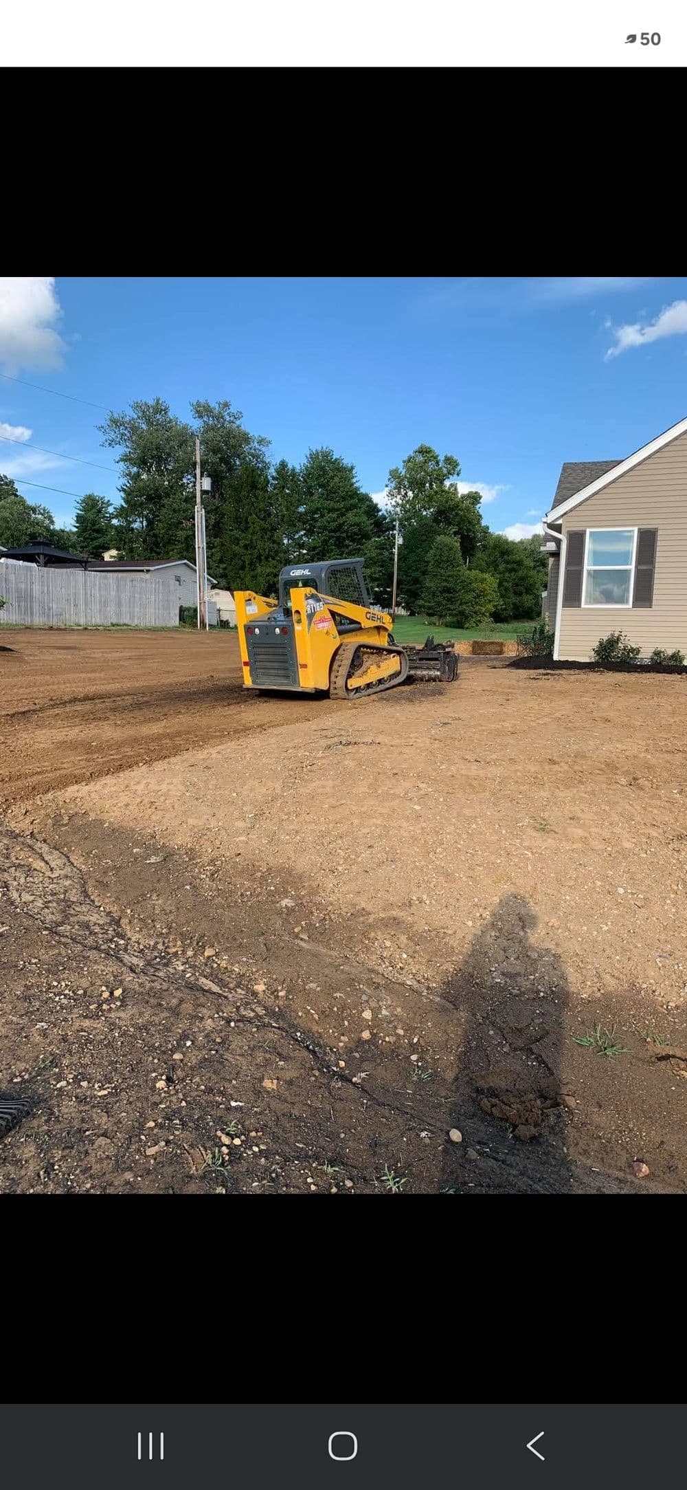 Yellow bulldozer leveling dirt on a construction site near a house under a clear blue sky.