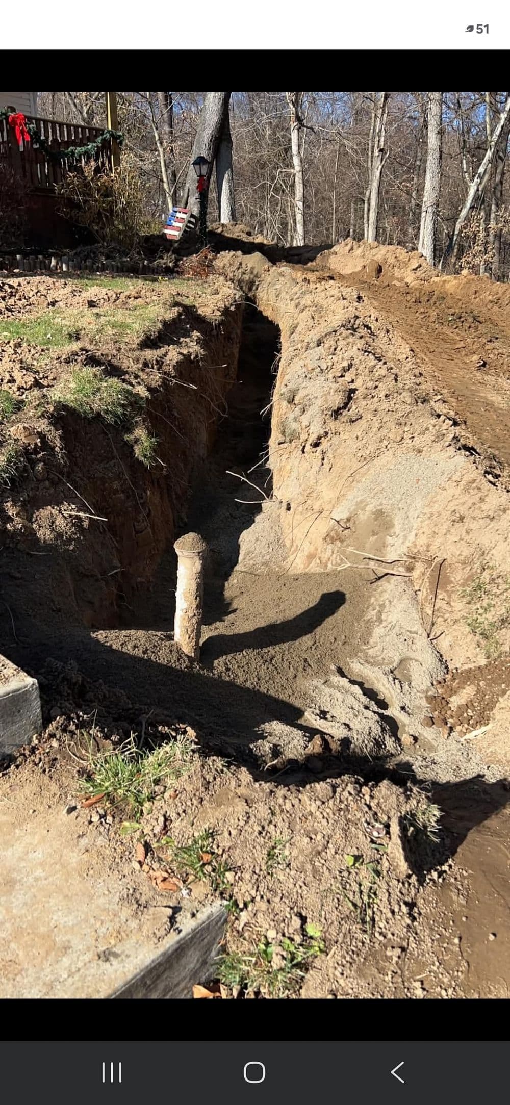 Excavated trench with exposed soil and a wooden post in a wooded area.