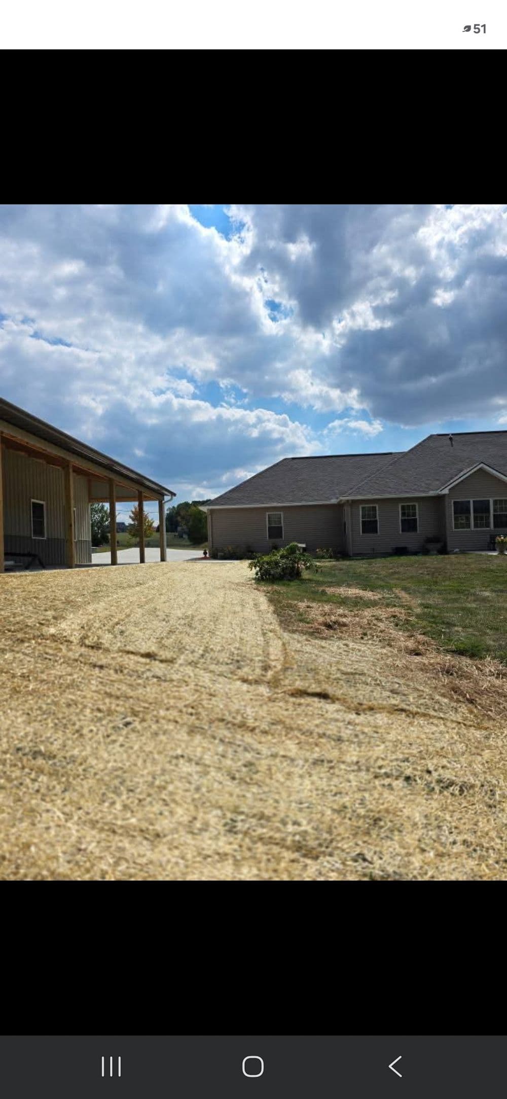 Driveway leading to two residential homes under a partly cloudy sky with green grass.