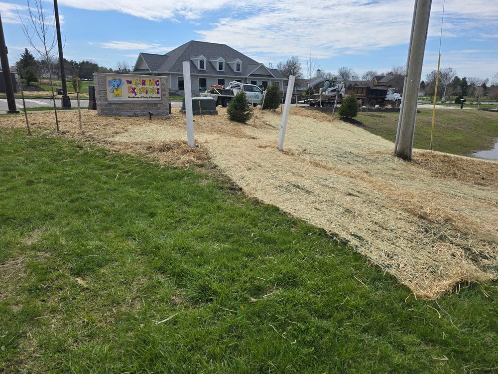 Newly mulched landscape at a residential property with sign, grass, and blue sky.