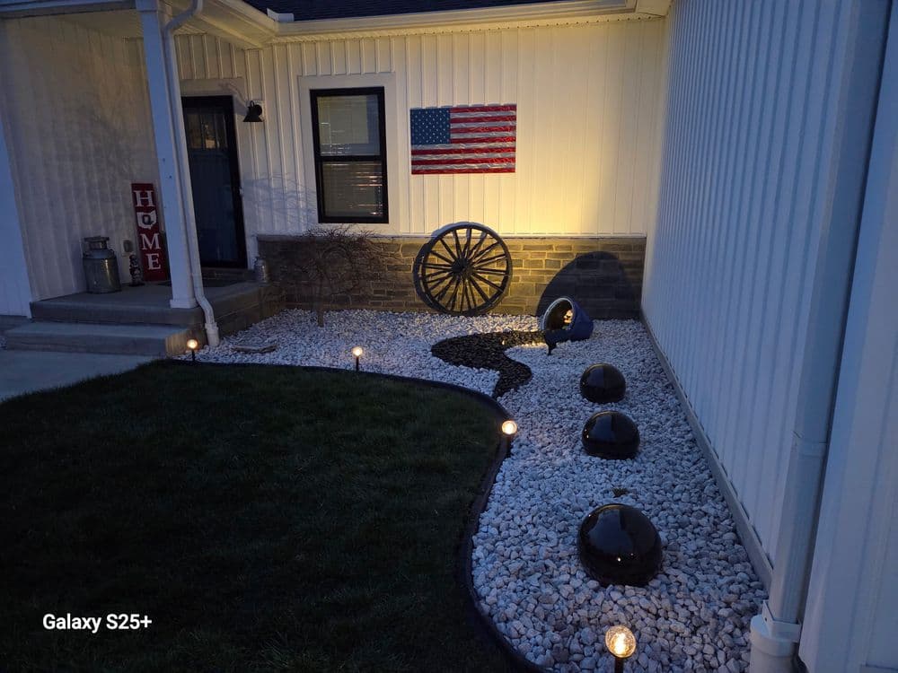 Landscape design featuring white gravel, decorative stones, and an American flag on the wall.
